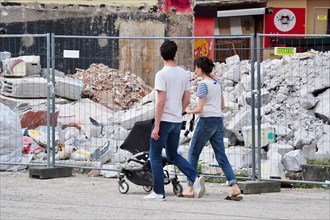 Young couple with pram in front of demolished house and barrier fence
