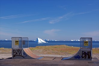 Skating rink painted with graffiti in front of icebergs floating in a bay