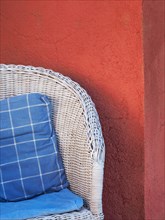 White wicker chair with blue and white checked cushion in front of red wall