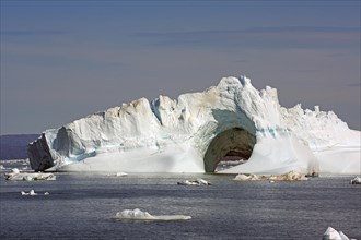 Small fishing boat in front of huge iceberg with two large caves