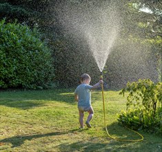 Toddler aged 3 playing with a water hose in the garden