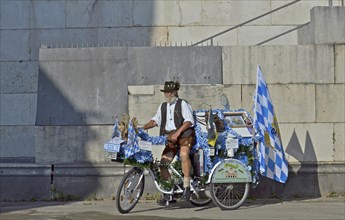 Man in Bavarian traditional costume on Bavarian decorated bicycle with white-blue Bavarian flag