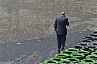 Man with mobile phone to ear in front of stacked car tyres at racecourse