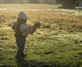 Toddler with teddy bear in the morning light in a meadow