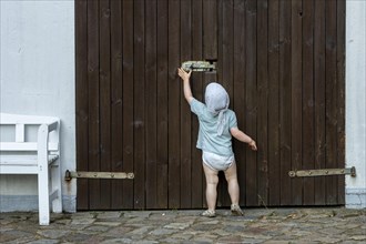 Toddler tries to move the security latch on a wooden door