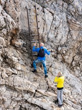 Tourists climb the metal ladder to the summit plateau of the Zugspitze