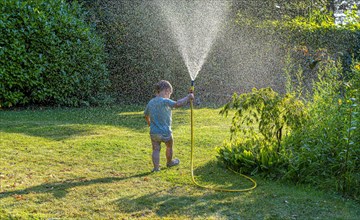 Toddler aged 3 playing with a water hose in the garden
