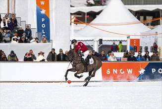 Spectators watch Max Charlton of Team St. Moritz galloping across the field with the red ball
