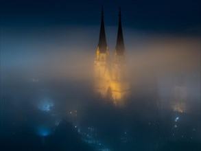 Illuminated church towers of Admont Abbey rise out of the fog