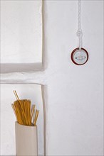 Spaghetti noodles in white container in front of white wall with old-fashioned light switch