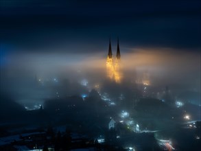 Illuminated church towers of Admont Abbey rise out of the fog