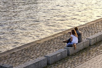 Young couple sitting to relax in the evening sun on the banks of the Spree in Mitte