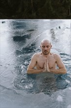 Man ice bathing in the pool folds his hands and meditates
