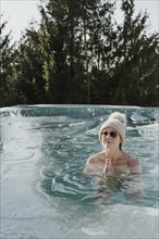Woman in cap folds hands while ice bathing in pool