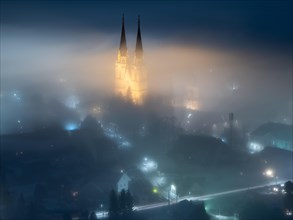 Illuminated church towers of Admont Abbey rise out of the fog