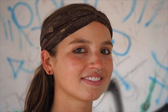 Young woman with forehead babd and nose piercing in front of graffiti wall