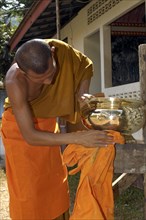 Buddhist monk cleans golden offering bowl in Buddhist monastery