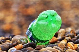 Green plastic bottle lying on pebble beach