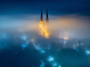 Illuminated church towers of Admont Abbey rise out of the fog