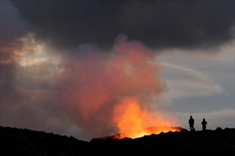 Tourists in front of reddish illuminated smoke cloud