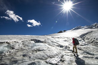 A climber with crampons and backpack walks across the sunlit Mera Glacier