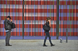 Man looking into bag and young woman talking on phone in front of colourful striped facade of Museum Brandhorst