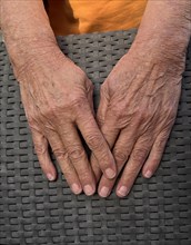 Wrinkled hands of an old woman on wickerwork of wicker chair