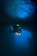 Diver dives with underwater lamp through rock grotto with blue light Blue Dome in Blue Hole of Gozo