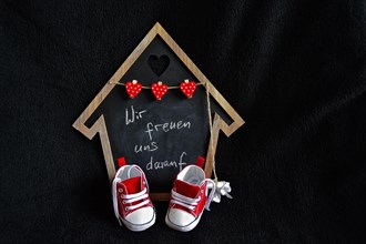 Black board as a house with red children's shoes and saying Wir freuen uns drauf