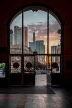 View out through the main entrance of a glass door of Frankfurt Central Station to the skyline in the romantic sunrise. A gateway to the city that is just waking up