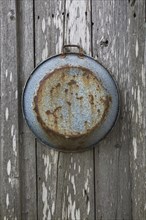 Old rusted pan hanging on grey weathered wall of old rustic wood plank cabin