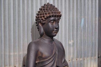 Sitting Buddha made of terracotta in front of a wall of corrugated iron