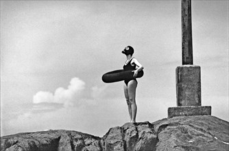 Young woman standing on rocks with gas mask and swimming tyre