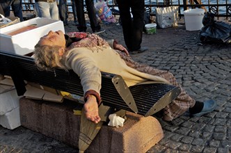 Sleeping homeless woman sleeping with outstretched arm on city bench