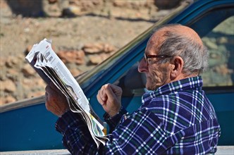 Old man with glasses reading newspaper in the street