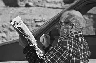 Old man with glasses reading newspaper in cafe