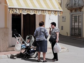 Conversation of two elderly woman on the street with baby in pram