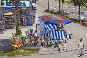 Fruit stand and kindergarten children with high visibility waistcoats