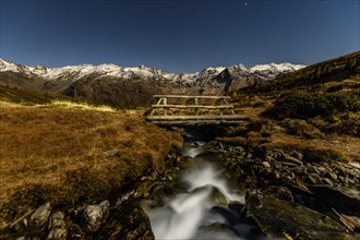 Mountain stream in moonlight with starry sky in autumnal landscape
