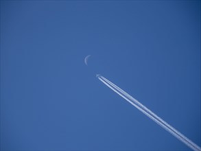 Aircraft with contrails and crescent moon
