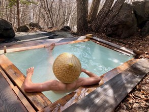 Young man with Japanese hat bathes in an onsen