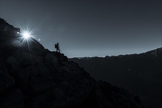 Mountaineer on rocky ledge with sun star