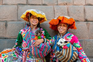 Two Inca woman in traditional traditional costume with lambs in front of an Inca wall