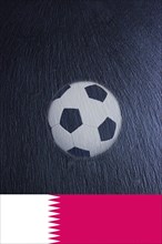 A football and the Qatar flag on a black slate