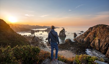 Young man looking at the sea and sandy beach Harris Beach with rocks at sunrise