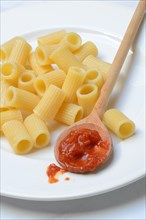 Cooked rigatoni and cooking spoon with tomato sauce