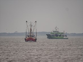 Crab cutter with ferry Spiekeroog IV on the stormy North Sea entering the harbour