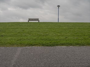 Grass-covered dyke under grey sky and tarred path
