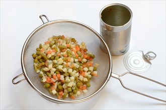 Russian salad in kitchen strainer and tin can