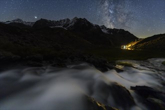 Mountain stream with Winnebachsee hut and Winnebach peaks with starry sky and Milky Way